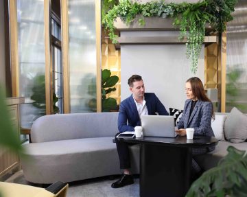 Two employees collaborating in an office space on a comfortable sofa, surrounded by greenery which depicts the future of the workplace.